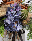 Decorative arrangement with blue flowers, cinnamon sticks, and greenery in a glass vase.