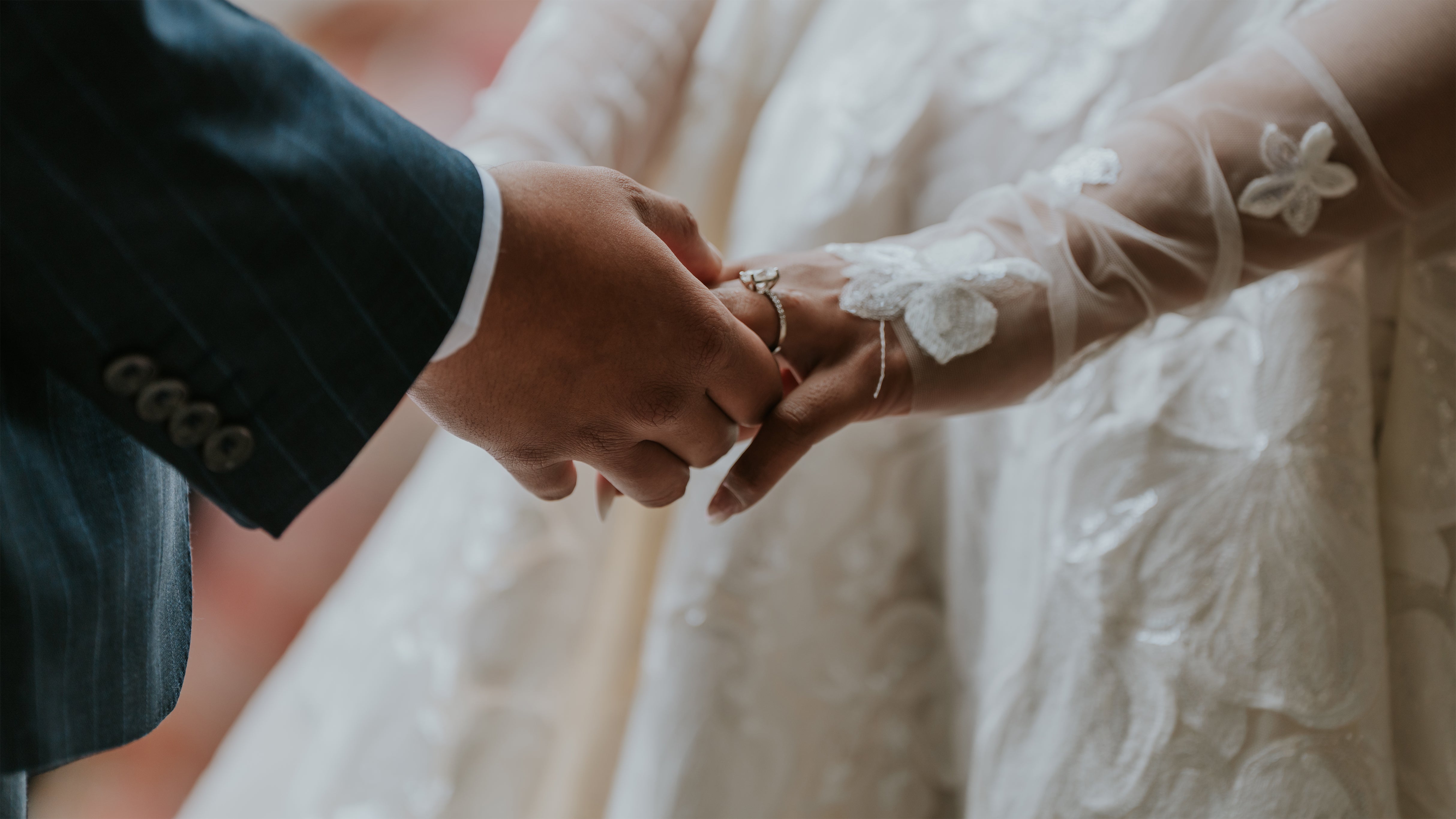 Close-up of bride and groom holding hands during wedding ceremony at Hampton Court Castle - Amaranté London, Wedding Event Florist