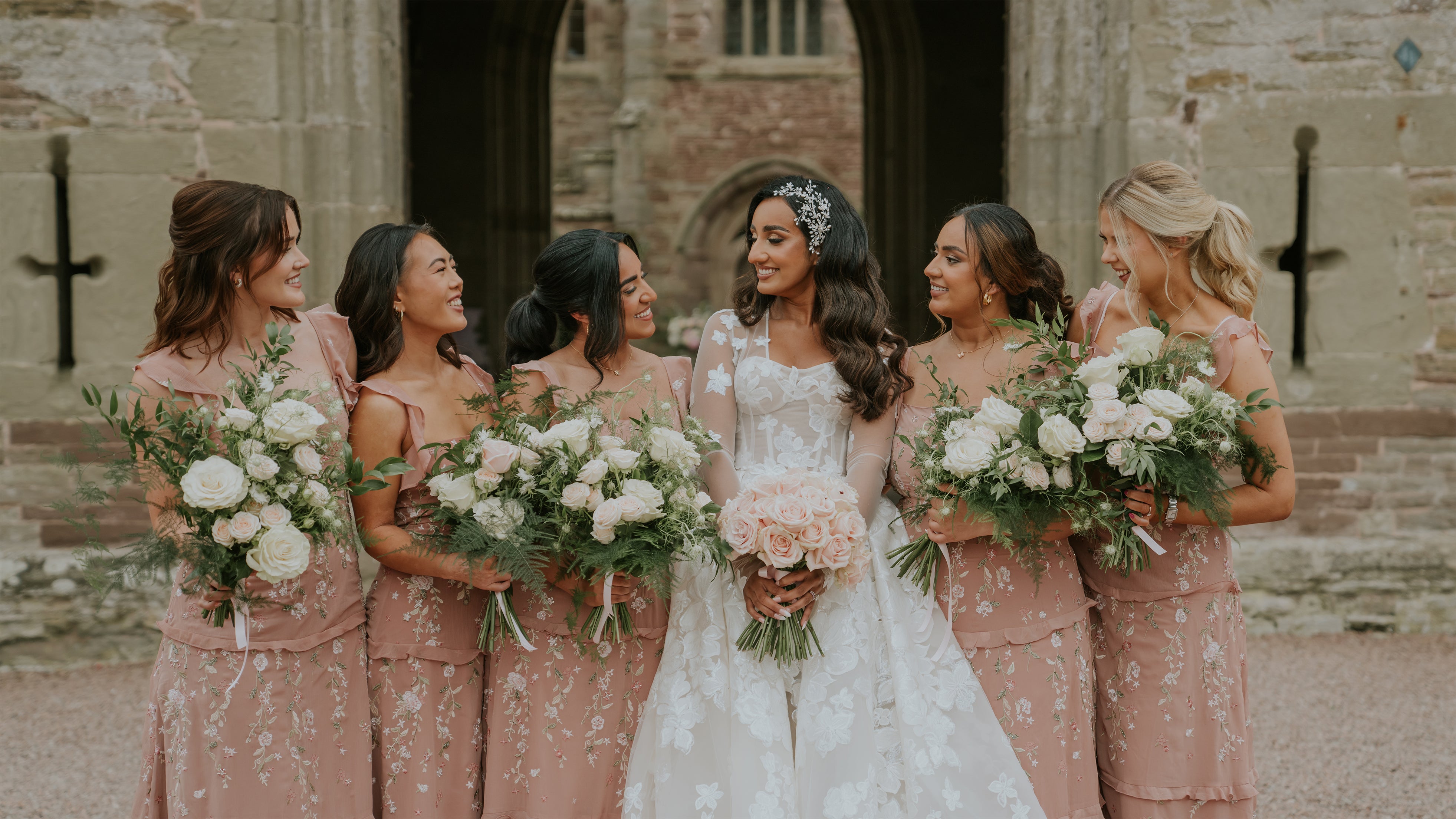 Bride and bridesmaids in blush pink dresses holding coordinated bouquets of white roses and eucalyptus greenery at Hampton Court Castle - Floral Design by Amaranté London.