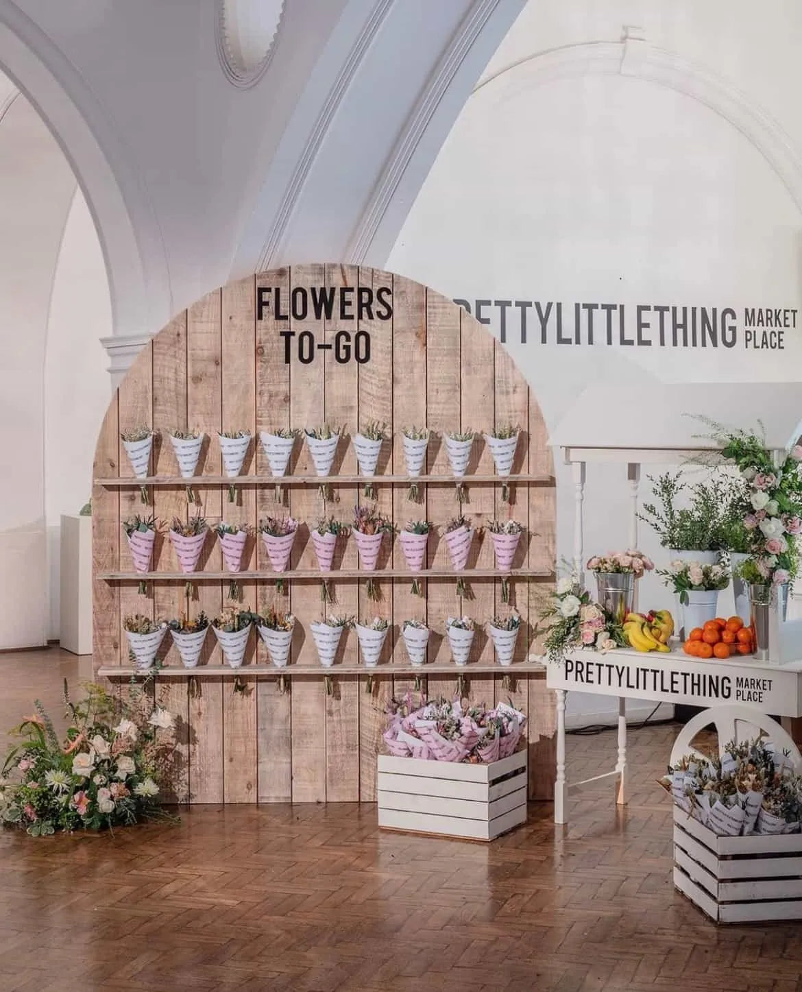 Prettylittlething - Corporate event floral installation featuring tiered wooden display with individual potted arrangements and branded signage, demonstrating Amaranté London's retail-style event production for brand activations