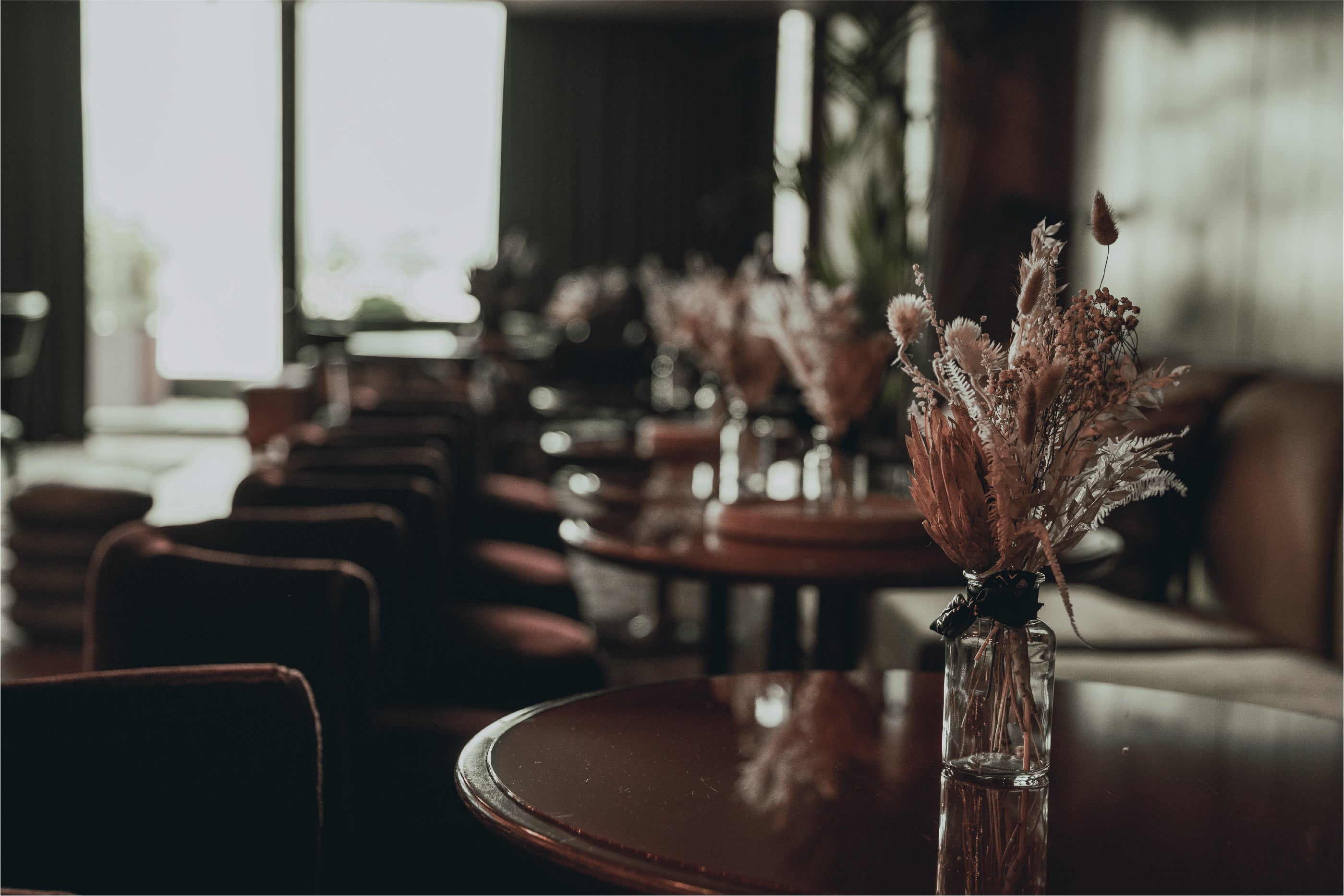 Amaranté's bespoke floral arrangements line the centre of polished mahogany tables, their blush and copper tones creating a warm, welcoming ambience, set against the luxurious backdrop of White City House's lounge with natural light streaming through large windows.