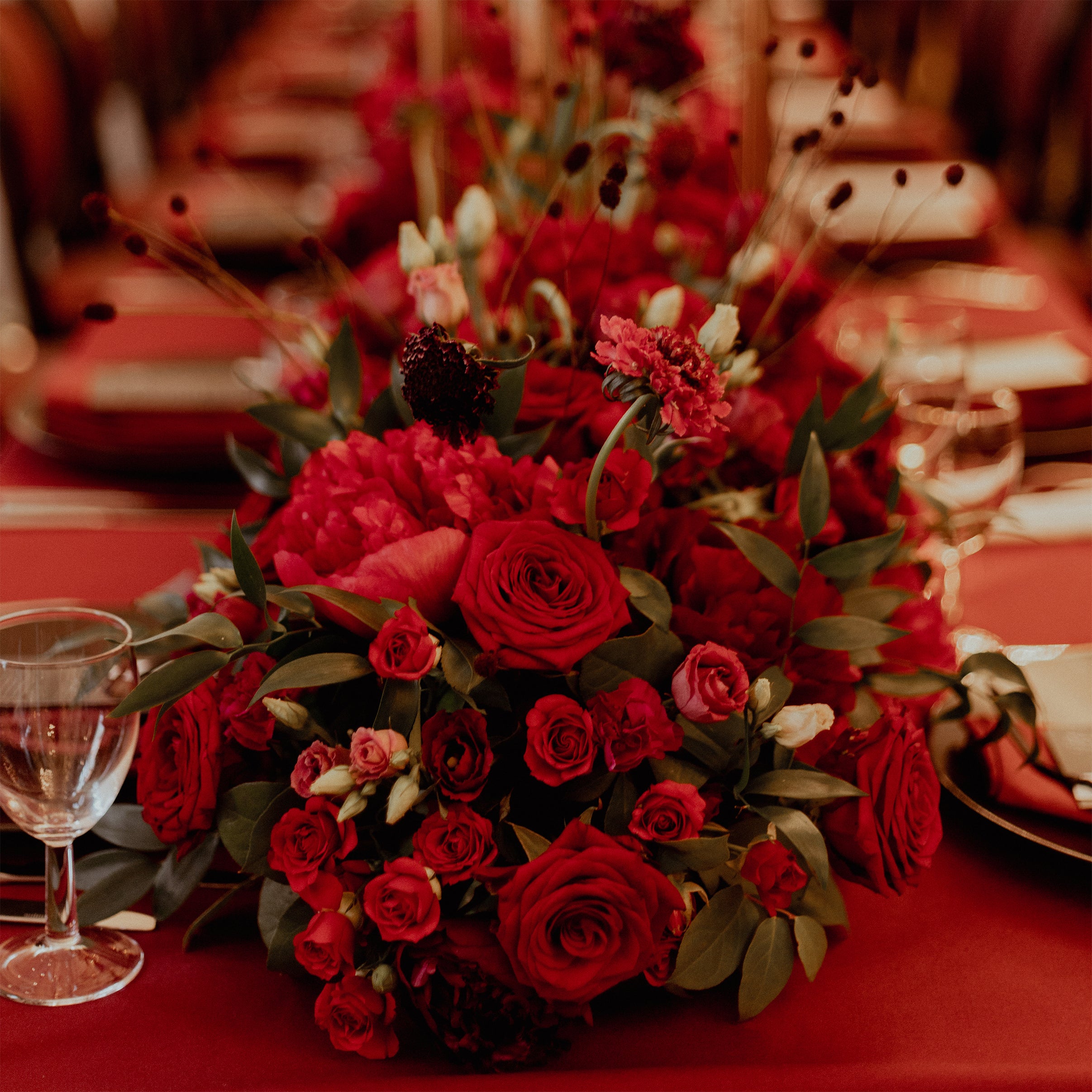 Luxurious red floral centerpiece at Waldorf Hilton with red roses, carnations, dahlias, and dark burgundy scabiosa creating a rich monochromatic display on the banquet table - Amaranté London.