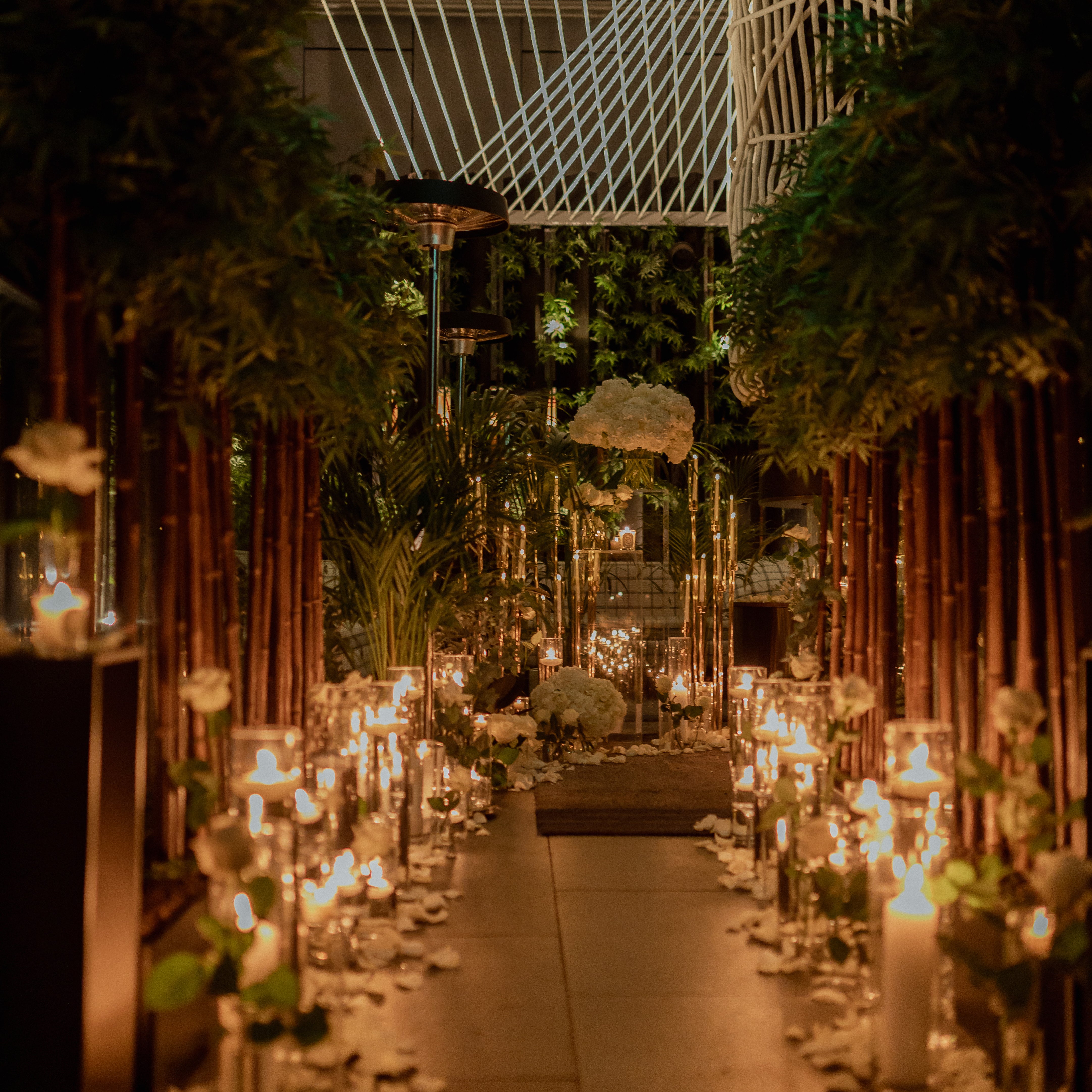 Dramatic proposal aisle with tall bamboo poles, floating candles, white hydrangea arrangements, and lush tropical greenery creating an enchanted garden atmosphere - Amaranté London