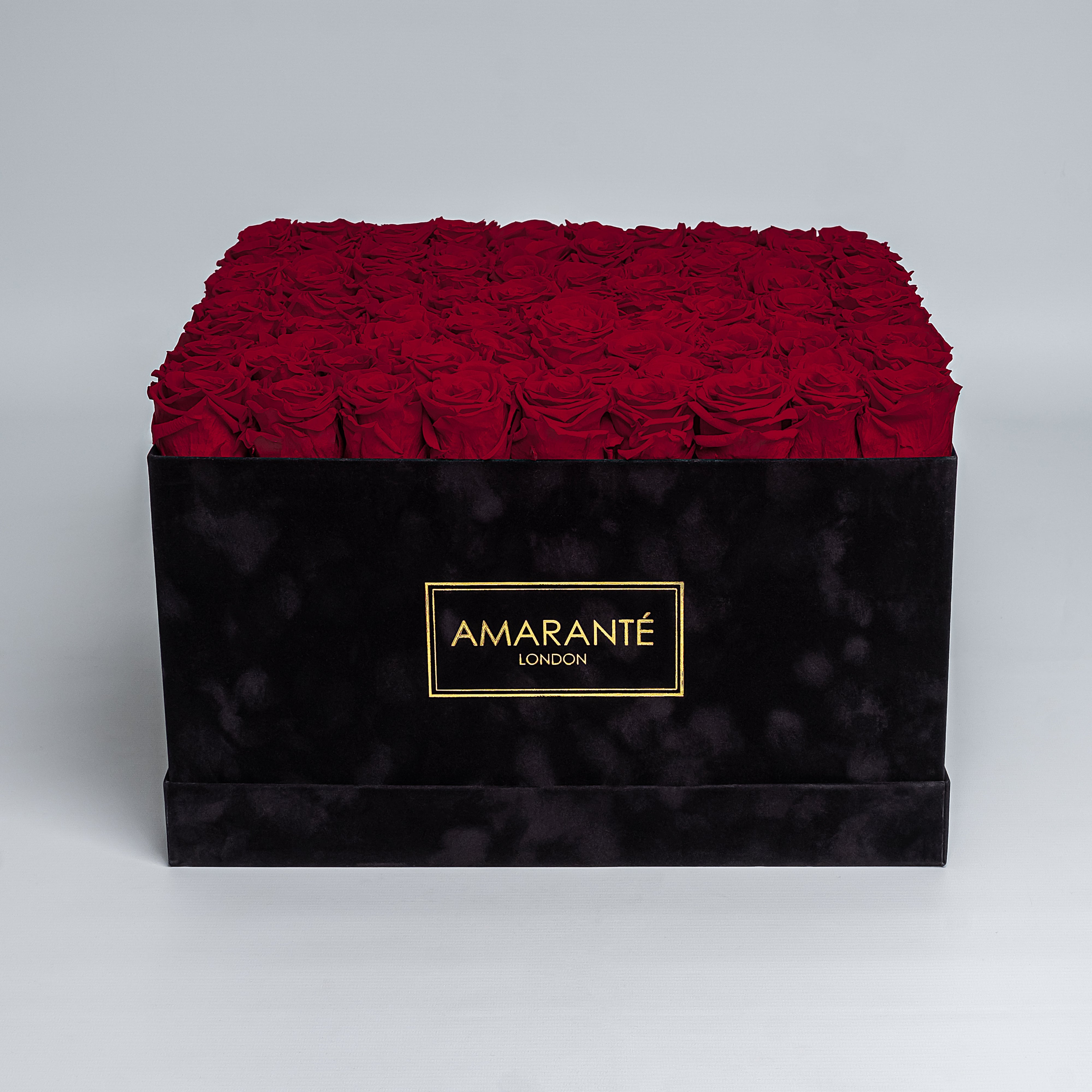 Luxurious square black suede box filled with 100 vibrant red roses, featuring the distinctive 'AMARANTÉ London' golden logo on the front.