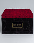 Luxurious square black suede box filled with 100 vibrant red roses, featuring the distinctive 'AMARANTÉ London' golden logo on the front.